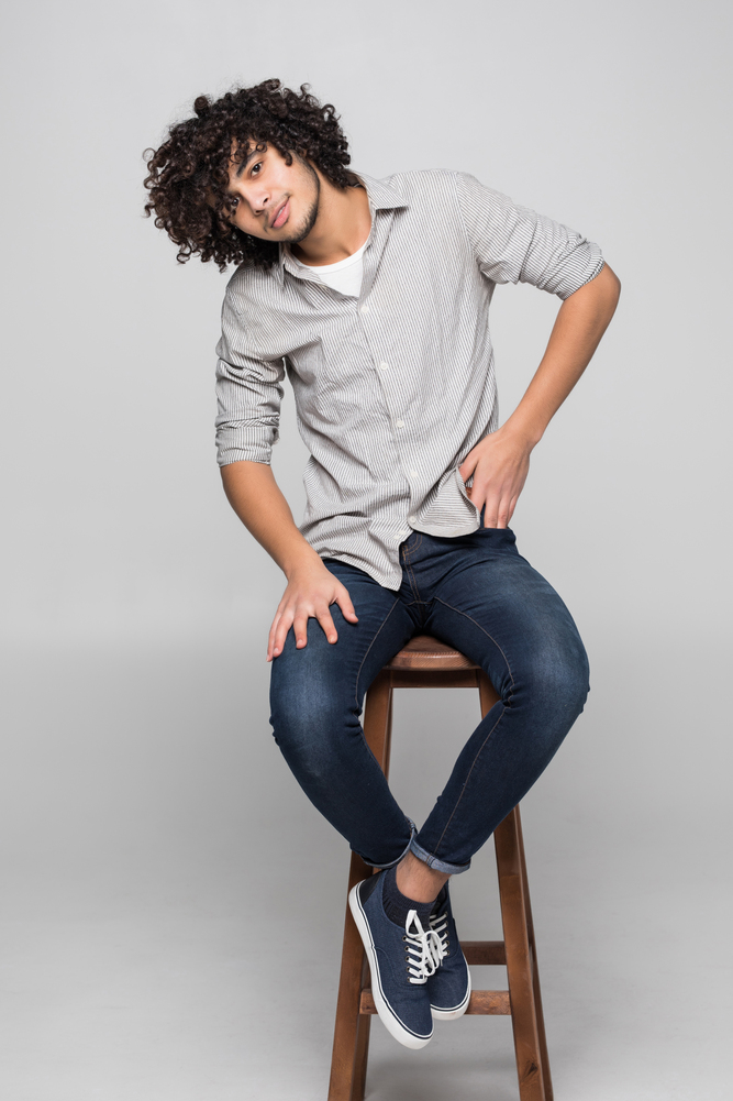 Young curly man sitting on a studio chair isolated on white background